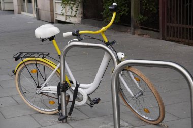 beyaz-sarı şehir bisikleti metropolün eski semtinde boş bir sokakta demir boru bir kablo ile park edilsin. insanlar için çevre dostu ve sağlıklı ulaşım modu. kaynak tasarrufu ve spor