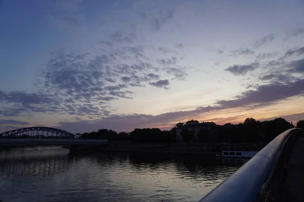 Nowoczesny most w świetle słońca, kolorowe niebo i chmury, miasto zachód słońca nad rzeką, woda. Wieczorna promenada, spacer. — Zdjęcie stockowe