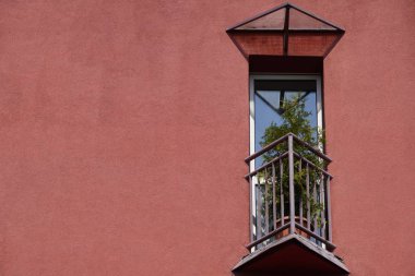 small triangular balcony in the house with a coral facade and potted flowers on fence. a place to rest your soul clipart