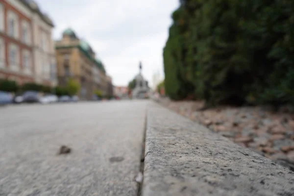 Paving slabs close-up on the background of streets, old buildings are in blur. Sharpness on granite tile. Square and houses are blurred in the background. Layout for design. The street is removed from — Stock Photo, Image
