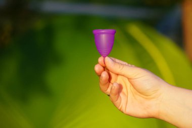 çadır arka planda kız elinde yakın çekim küçük mor adet Kupası. . Kadın sağlığı için çevre dostu bir kavram. Menstrüasyon için jinekolojide yenilik ürünü. çevre dostu, sıfır atık