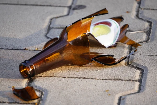 Fles bier, soda of drugs van donker glas is gebroken. Shattered bier fles op de grond in zonsondergang licht. Fragmenten van glas op asfalt. Textuur, achtergrond, wallpaper. — Stockfoto