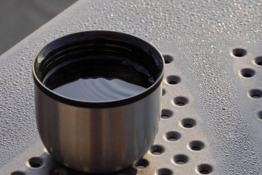 Sıcak içecek ve kuru üzümlü yulaf kurabiyesi ile termos fincan, kamp çay masada. sabah çiy, masada su damlaları, yumuşak gündoğumu veya günbatımı ışık, arka plan