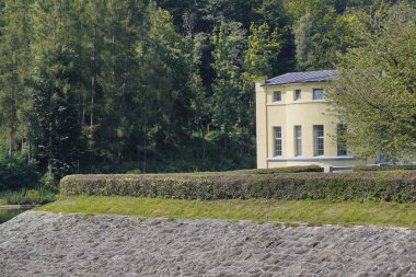 ormana karşı bir tepe üzerinde bir kale şeklinde inşaat, kıyı büyük taşlar, eskrim ile kaplı.