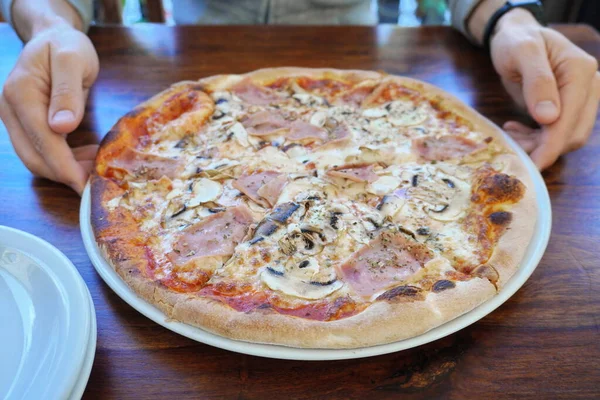 Bir adam koca bir pizzayı tabakta tutar. İtalyan mutfağı, fırında pişmiş. Lokantada lezzetli yemekler servis ediliyor. — Stok fotoğraf