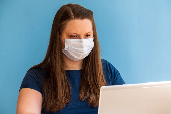 woman in medical mask works at home at computer during quarantine due to coronavirus. Prevention of respiratory diseases.Remote work quarantine, work from home or balcony in black grasses.