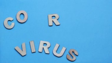 Coronavirus, mavi arka plandaki ahşap harflerden oluşur. Mektuplar arka planda birer birer kayboluyor. Hareketi durdur.