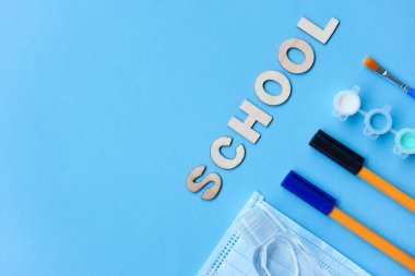 Düz konsept çalış. Eğitim malzemeleri - kalem, fırça, boya, tıbbi maske ve dezenfekte boyası mavi arka planda, okula ya da anaokuluna geri dönmek. Yaz zamanı, yaratıcılık ve öğrenme geçmişi