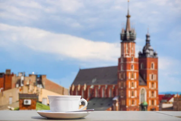 Cup of coffee with view of Church Bazylika Mariacka or towers of st.Mary's. Top view from roof or balcony to old Krakow,Poland town, market square. Sunny warm day, blue sky with clouds