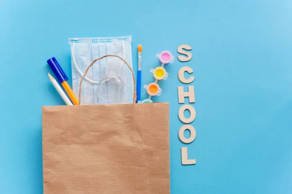 Study flatly. Education supplies-pencil,pen,brush, paint, medical mask and sanitizer paint on blue background,back to school or kindergarten.buying in eco bag, creativity and learn background with