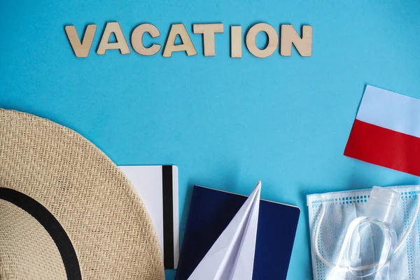 Top view hat,mask, sanitizer, passport, credit card, paper airplane on blue. Relax on coronavirus. Summer flatley, composition with copy space,travel and leisure concept. Wooden word Vacation, polish