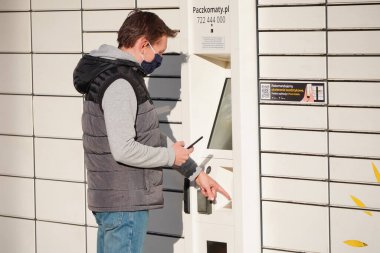 Krakow, Polonya 21.04.2020: Mavi maskeli genç bir adam paketler için Kutular 'dan bir paket aldı. Koronavirüs salgını sırasında mal ve ürünlerin temassız ya da temassız teslimatı.