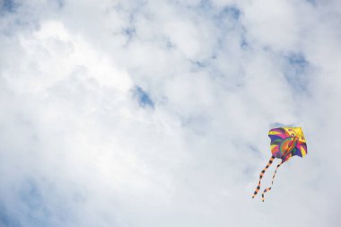 Mavi gökyüzünde beyaz bulutlu parlak, renkli bir uçurtma