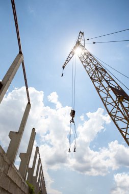 Güneşli bir gökyüzünün arka planında inşaat halindeki bir binanın yanında büyük bir vinç var.
