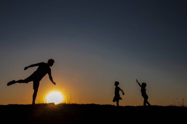 Güneş batarken çekilmiş eğlenceli, sembolik bir fotoğraf. Bir baba ve çocuğun futbol oynadığı bir balo.