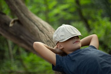 Oğlan ormanda dinleniyor, bir ağaç gövdesine yaslanıyor, elleri başının arkasında, şapkası gözlerinin üstüne çekilmiş. Yüzünde mutlu, tatmin olmuş bir gülümseme