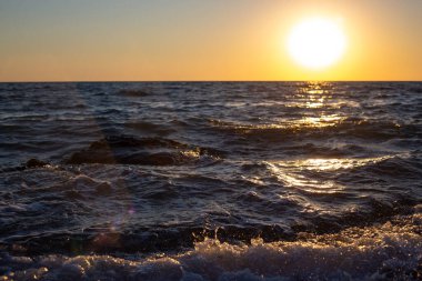 Denizin üzerinde gün batımı, dalgaların sularla dalgalandığı deniz kıyısı.