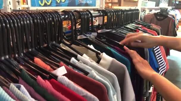 Il primo piano di mani femminili ha strappato una gruccia con vestiti. Le mani di una donna corrono su una rastrelliera di vestiti. Dolly ha sparato da un lato. mano della donna lisciatura un vestiti colorati. Primo piano una gruccia per abbigliamento — Video Stock