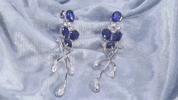 Zwei goldene Saphir-Ohrringe mit kleinen Diamanten. Paar Platin-Ohrringe mit Saphir-Edelstein auf blauem Satinhintergrund. Luxuriöser weiblicher Schmuck, Nahaufnahme — Stockvideo