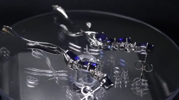 Dois brincos de safira dourada com diamantes pequenos. Par de brinco de platina com pedra preciosa de safira no fundo de cetim azul. Jóias femininas de luxo, close-up — Vídeo de Stock