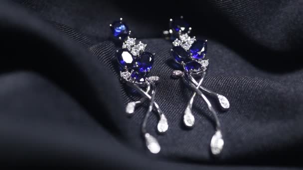 Två gyllene safirörhängen med små diamanter. Par av platina örhänge med safir ädelsten på blå satin bakgrund. Lyxiga kvinnliga smycken, närbild — Stockvideo