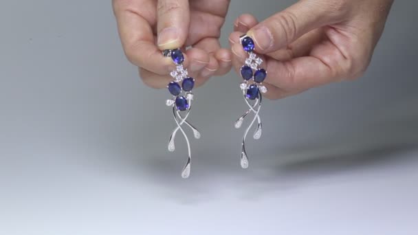 Dois brincos de safira dourada com diamantes pequenos. Par de brinco de platina com pedra preciosa de safira no fundo de cetim azul. Jóias femininas de luxo, close-up — Vídeo de Stock