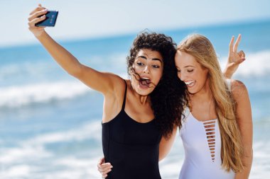 İki genç kadın selfie fotoğraf akıllı telefon ile Mayo içinde tropikal bir kumsalda alarak..