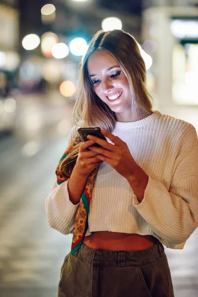 Mujer Rubia Mirando Teléfono Inteligente Calle Luces Desenfocadas Ciudad Fondo — Foto de Stock