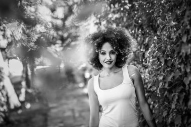Genç kadın kentsel parkta gülümseyen afro saç modeli ile siyah. Karışık kız rahat kıyafetler giyiyor. Siyah ve beyaz fotoğraf.