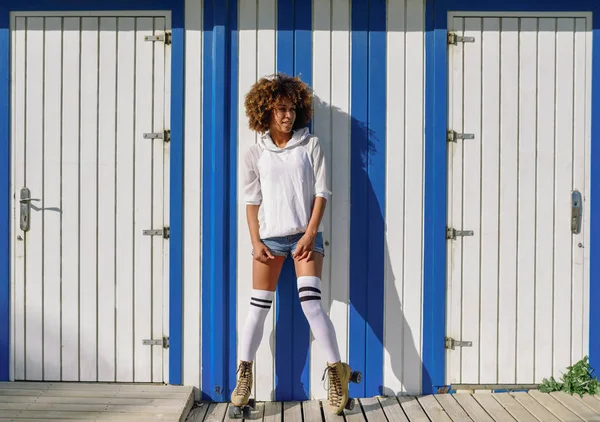 ビーチの小屋の近くのローラー スケートで若い黒人女性 日当たりの良いプロムナードにアフロの髪型ローラーブレードを持つ少女 — ストック写真