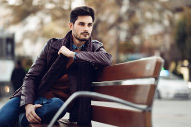 Kentsel bir bankta oturan düşünceli genç adam. Çekici adamla sokakta kayıp bakışla modern saç modeli.