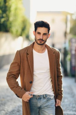 Sokağın ortasında kış giysileri giyen genç adam. Genç adam ceket, kot ve beyaz t-shirt ile modern saç modeli ile sakallı.