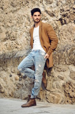 Sokağın ortasında kış giysileri giyen genç adam. Genç adam ceket, kot ve beyaz t-shirt ile modern saç modeli ile sakallı.