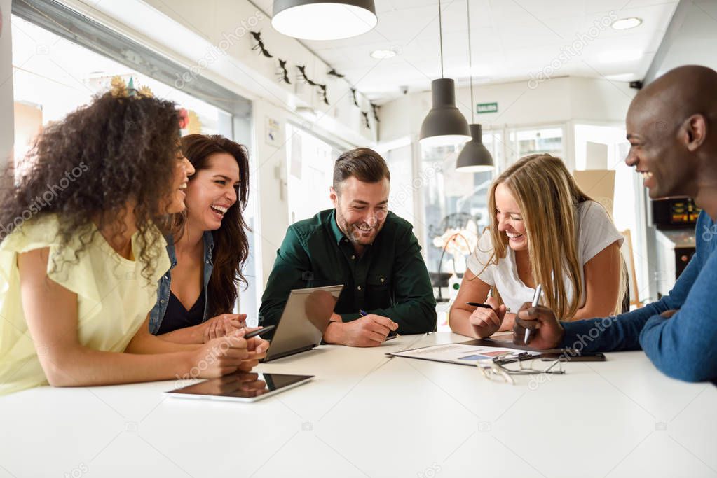 Five young people studying with laptop and tablet computers on white desk. Beautiful girls and guys working toghether wearing casual clothes. Multi-ethnic group smiling.