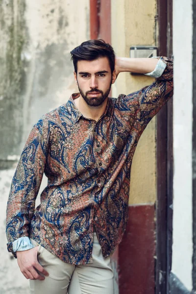 Young bearded man, model of fashion, wearing modern shirt in the street. Guy with beard and modern hairstyle in urban background.