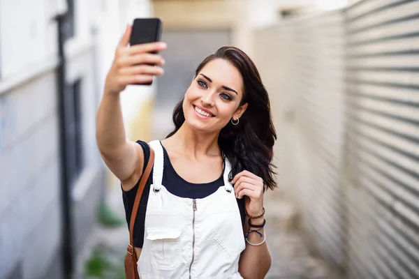 若い女性は彼女のスマート フォンと Selfie 写真を屋外撮影します 都市の背景にデニムのドレスを着ている少女 技術コンセプト — ストック写真