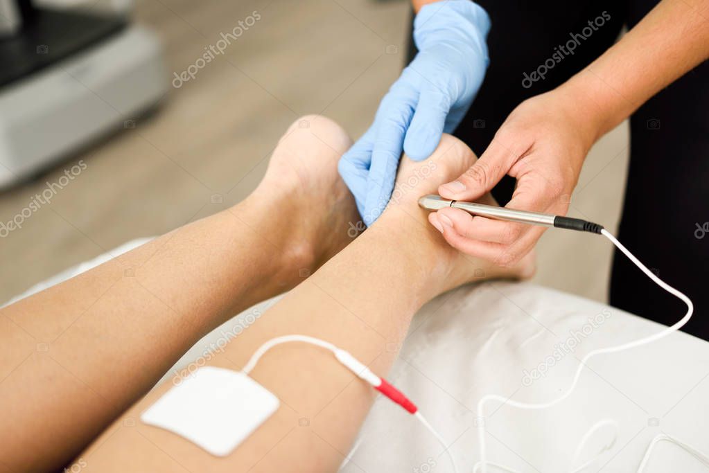 Electroacupuncture dry with needle connecting machine used by acupunturist on female patient for acupuncture guided by EPI Intratissue Percutaneous Electrolisis. Electro stimulation in physical therapy to ankle of a young woman in physiotherapy cente