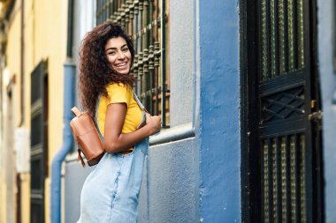 Genç Kuzey Afrikalı kadın, moda, siyah kıvırcık saç modeli açık havada ile modeli. Kentsel sokakta rahat kıyafetler içinde gülümseyen Arap kız.