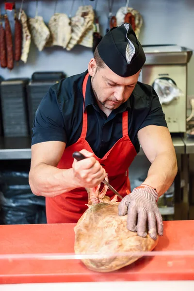 Male butcher boning a ham in a modern butcher shop with metal safety mesh glove