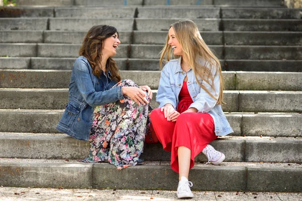 Two young women talking and laughing on urban steps. Two girls wearing casual clothes. Lifestyle concept.