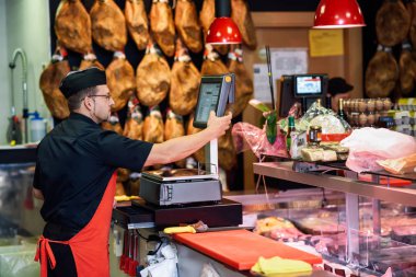 Kasap et ağırlıklı bir kasap dükkanında ve arka plan, jambon ile şarj
