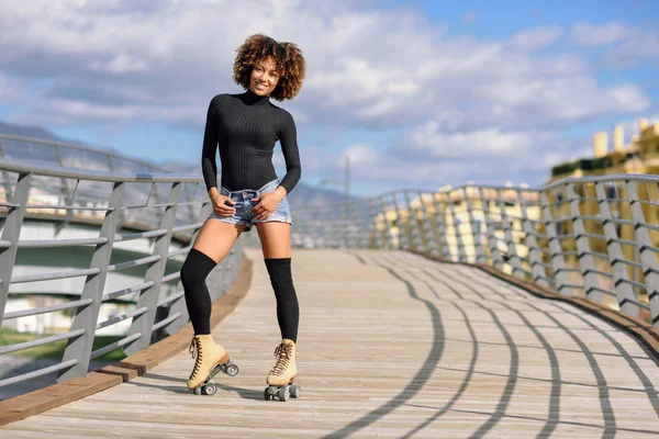 黒人女性で ローラー スケートに乗って両手を広げて都市橋屋外で アフロの髪型 晴れた日に若い女性のローラーブレードを笑っています 空には美しい雲 — ストック写真