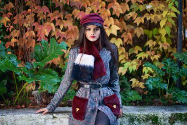 Çok uzun saçlı, sonbahar yapraklarında kışlık palto ve şapka giyen genç ve güzel bir kız. Yaşam tarzı ve moda konsepti.