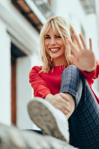 Feliz Joven Rubia Sentada Fondo Urbano Poniendo Mano Cerca Cámara — Foto de Stock