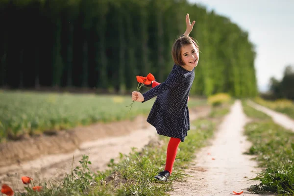 彼女は手に花ドレス着て美しい自然フィールドで歩いている女の子 — ストック写真