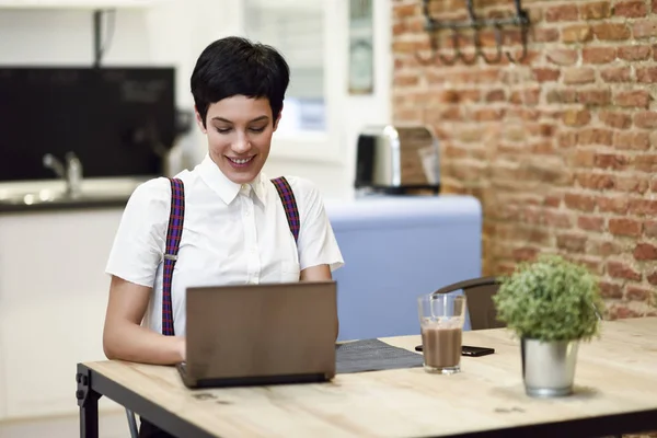 Ung kvinna med mycket kort frisyr att skriva med en bärbar dator hemma. — Stockfoto