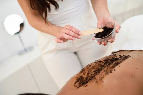 Kobieta oczyszcza skórę ciała z peelingu kawowego w centrum odnowy biologicznej spa. — Zdjęcie stockowe