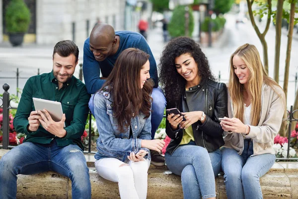 Jeunes multiethniques utilisant des smartphones et des tablettes à l'extérieur — Photo