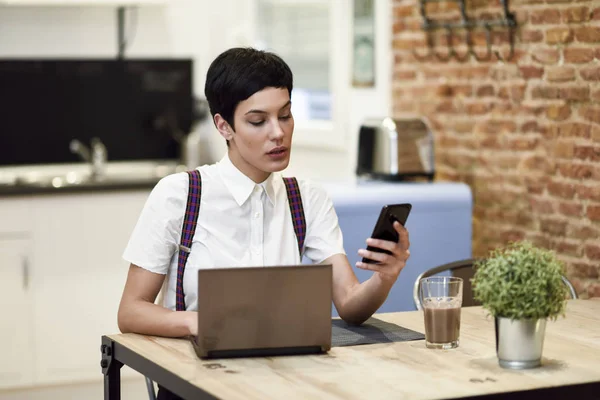 Ung affärskvinna med mycket kort frisyr tittar på hennes smartphone hemma. — Stockfoto