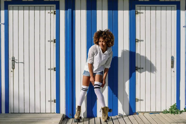 Joven mujer negra en patines cerca de una cabaña de playa . —  Fotos de Stock